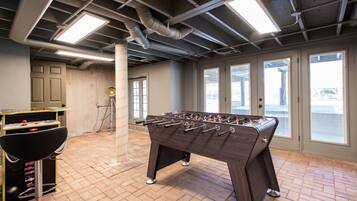 A room with a foosball table, a pool table, and a bar area with stools.