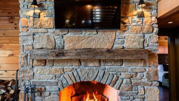 Ein Kamin aus Stein mit einem darüber angebrachten Fernseher, ein Feuer im Inneren und eine Holzbalkendecke.