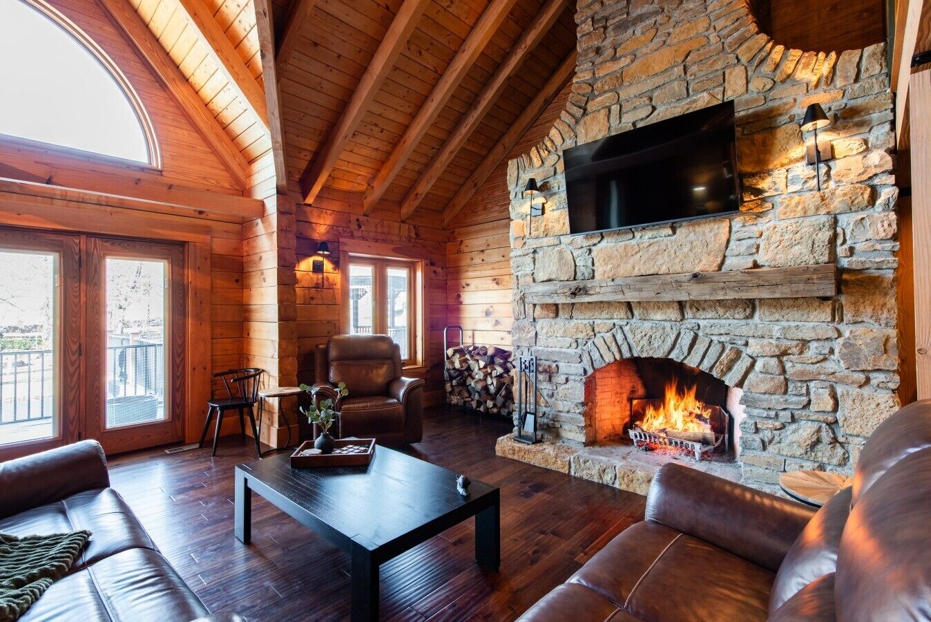 A cozy room with a stone fireplace, leather furniture, and a flat-screen TV mounted on the wall.