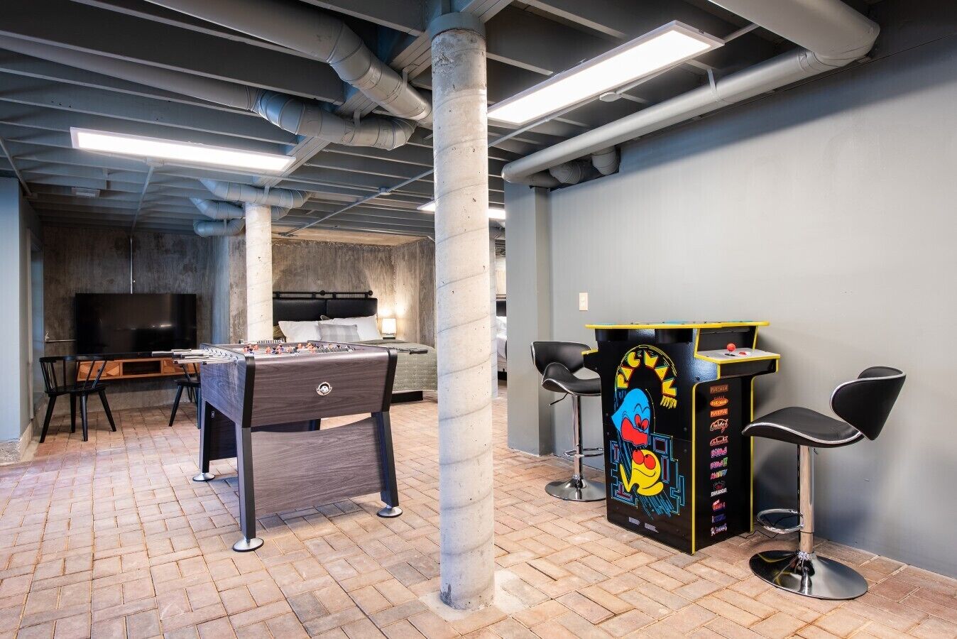 A room with a foosball table, a TV, and a bar area with stools.