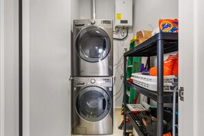 Ein Waschraum mit zwei übereinandergestellten Waschmaschinen mit Frontöffnung, einem Stromzähler und Regalen mit Reinigungsmitteln.