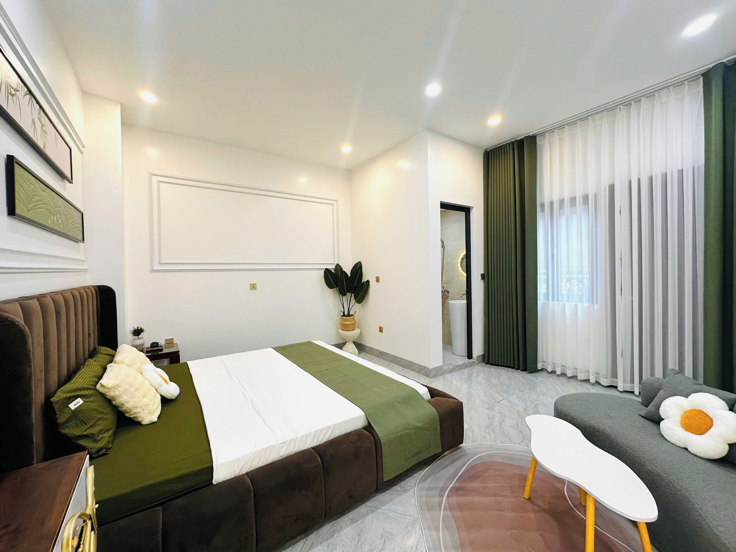 A modern bedroom with a bed, a sofa, a small table, and a potted plant.