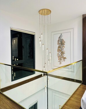 A modern interior with a glass railing, a hanging light fixture, and a wall-mounted decorative piece.
