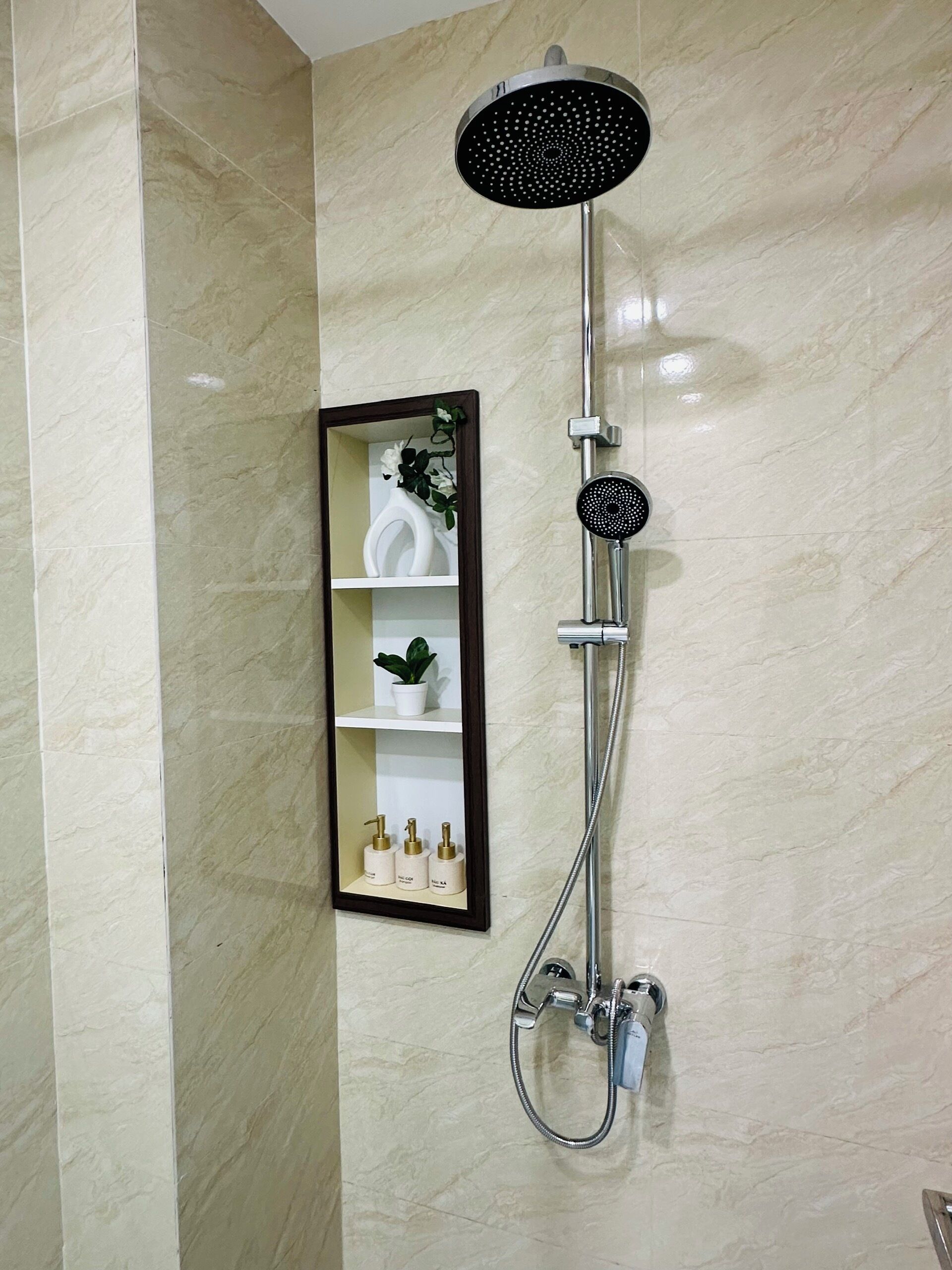 A bathroom with a wall-mounted shower, a mirror, and a shelf with toiletries.