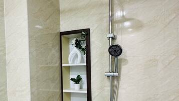A bathroom with a wall-mounted shower, a mirror, and a shelf with toiletries.