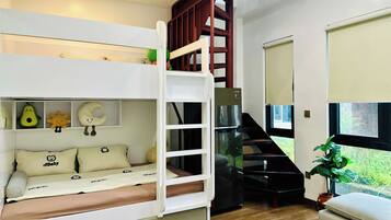 A bunk bed with a wooden ladder, a desk, and a chair. There is a window with a view of greenery.