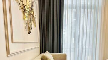 A modern living room with a beige sofa, a decorative wall piece, and a large window with sheer curtains.