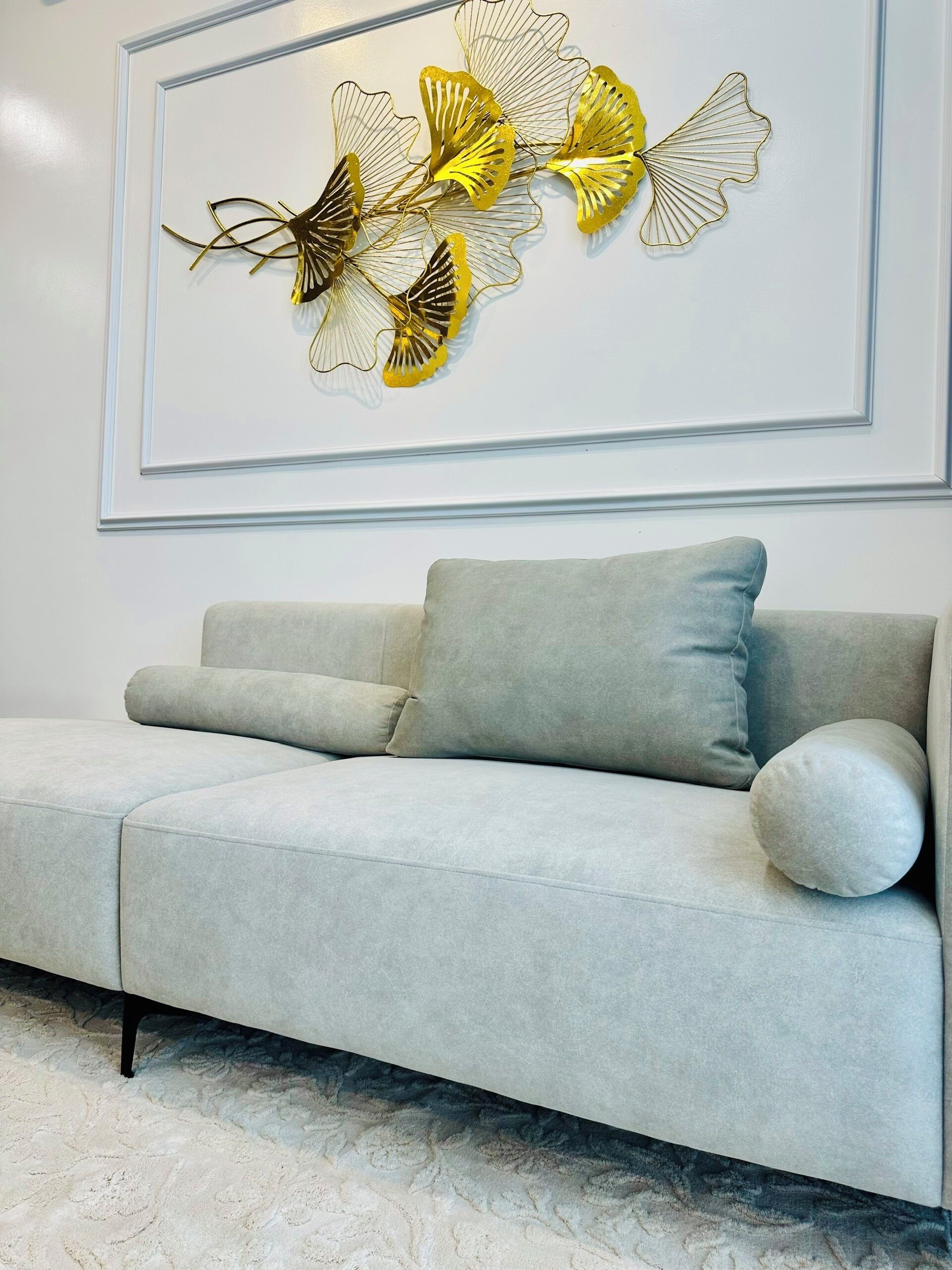 Um sofá cinza claro com uma almofada e um objeto decorativo na parede acima.