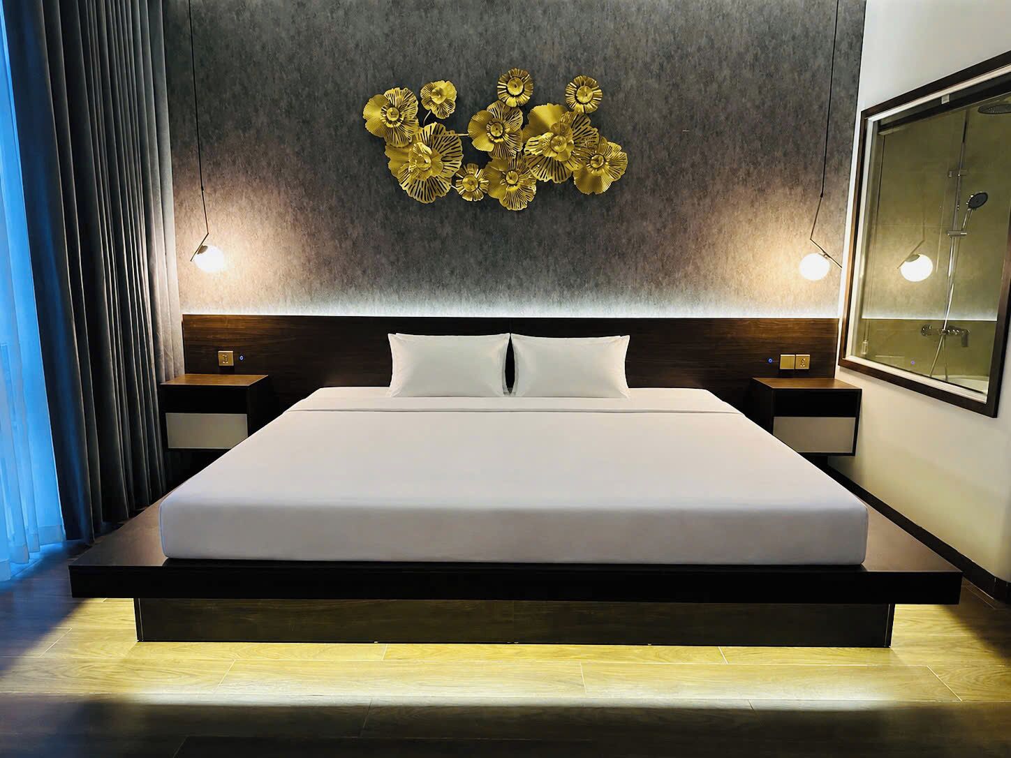 A modern hotel room with a large bed, a wall-mounted decorative piece, bedside lamps, and a view of the bathroom.