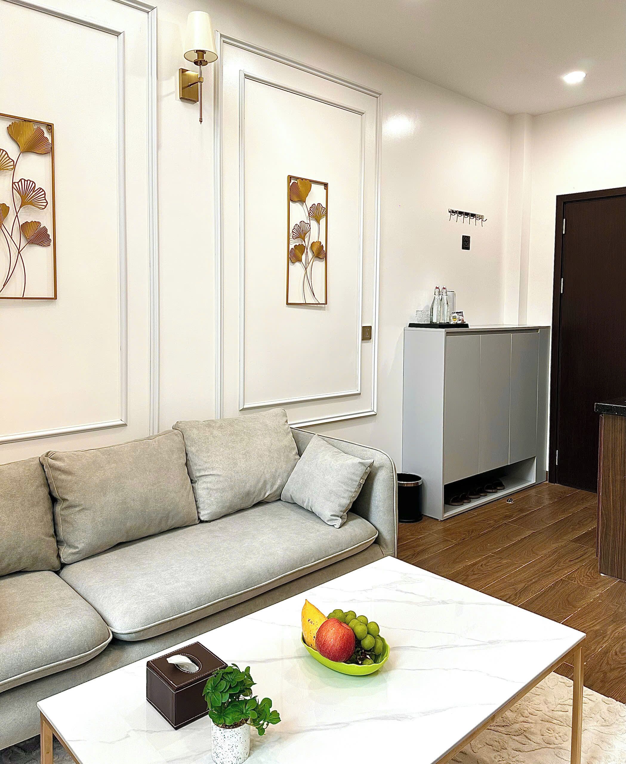 Una sala de estar moderna con un sofá gris, una mesa de centro blanca con una planta y un frutero, y obras de arte en las paredes.
