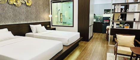 A hotel room with two beds, a large window, a kitchen area, and a bookshelf.