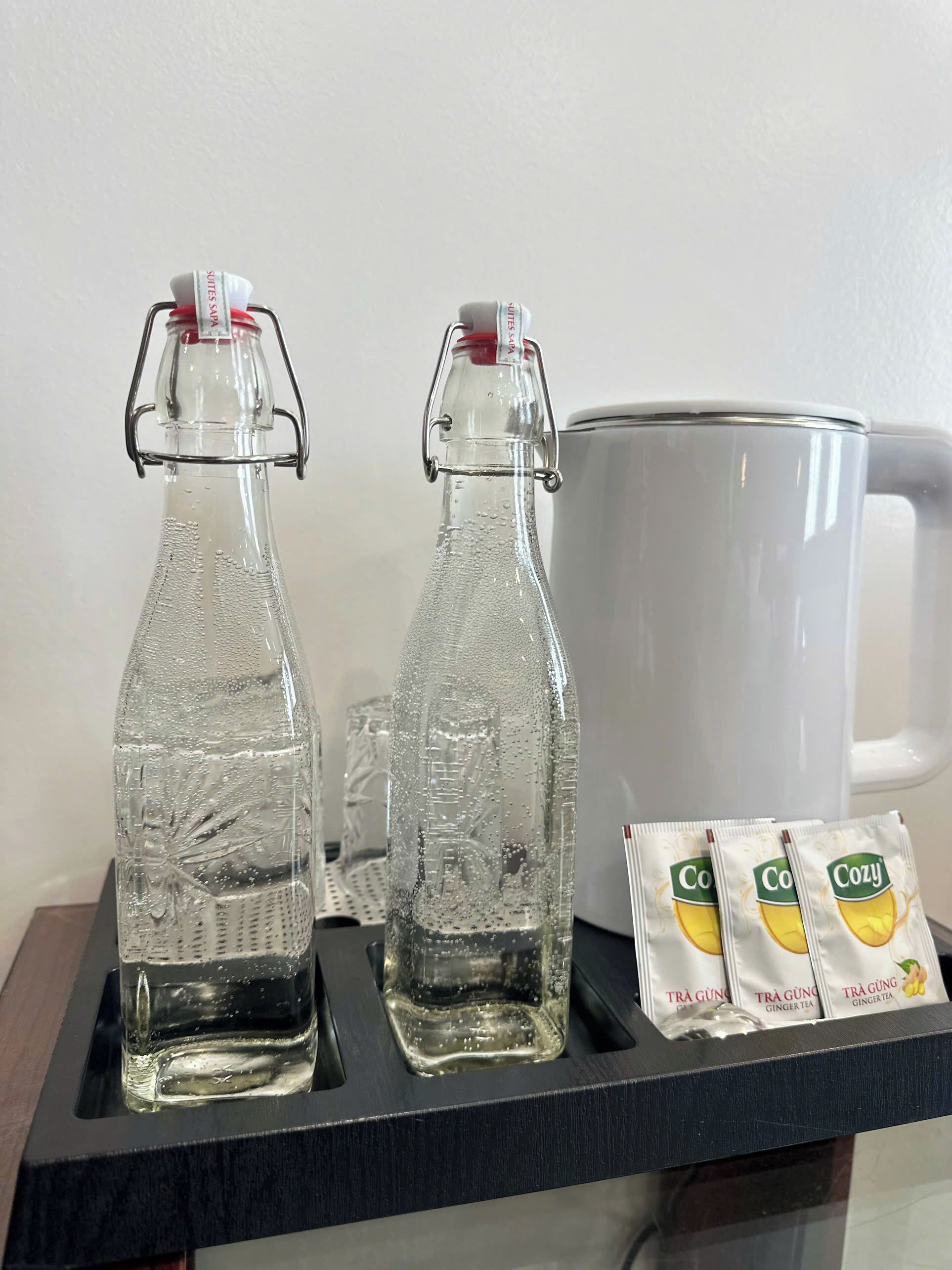Dos botellas de vidrio con cierres metálicos, una taza blanca y bolsitas de té de jengibre sobre una bandeja.