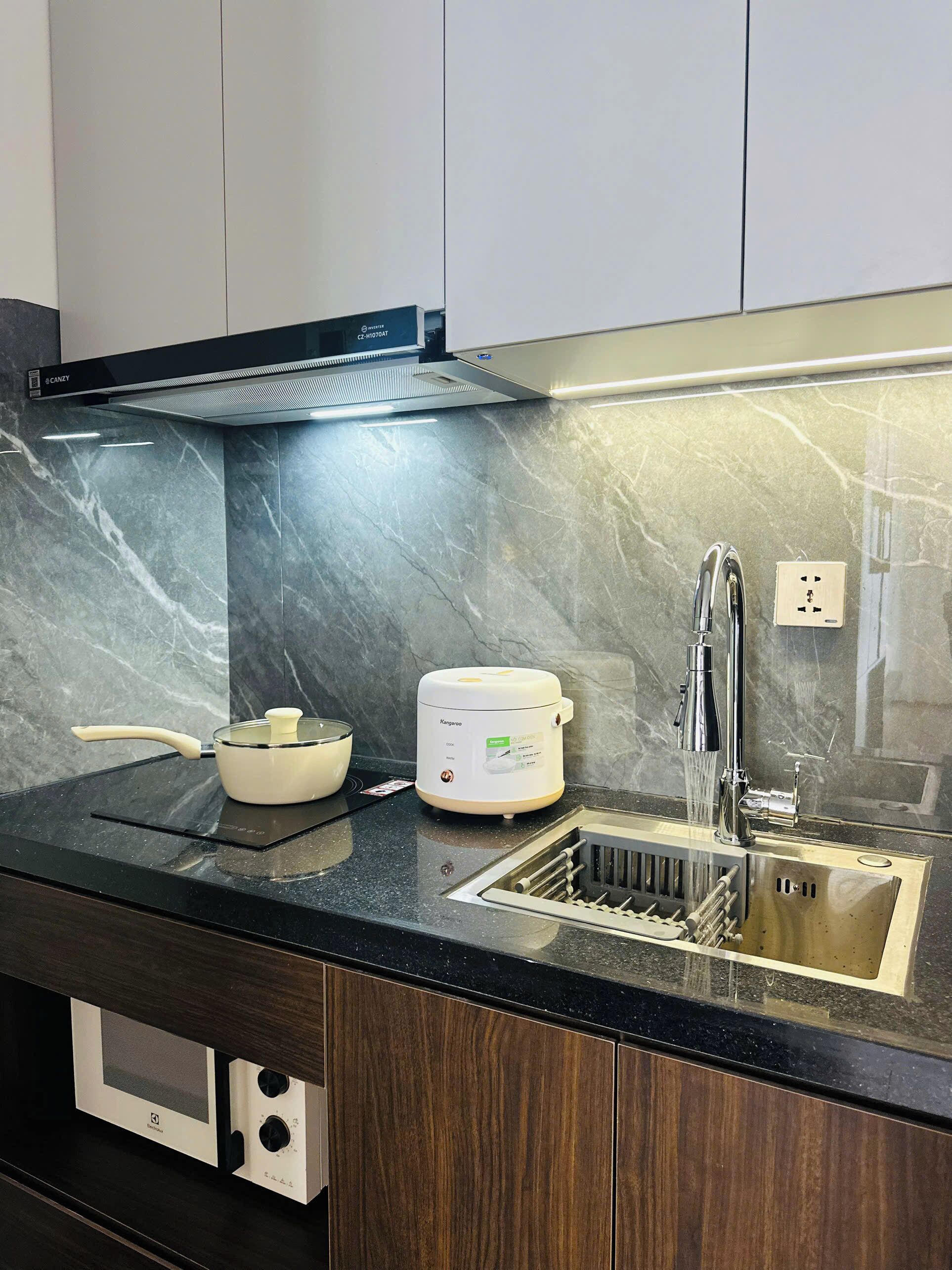 A modern kitchen with a built-in stove, a rice cooker, and a stainless steel sink.