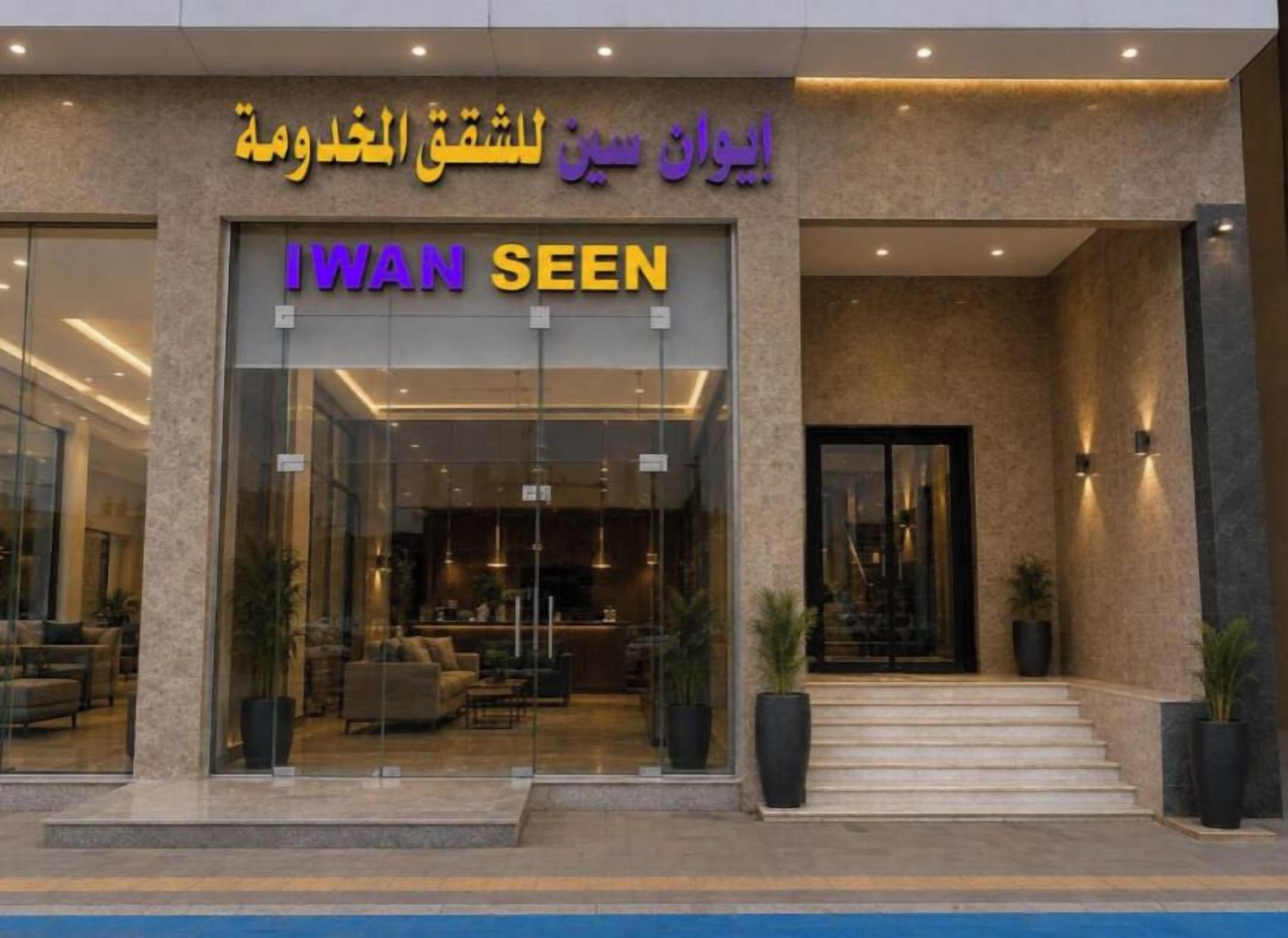 A hotel entrance with a glass facade, a sign reading 'IWAN SEEN', and a staircase leading to the entrance.