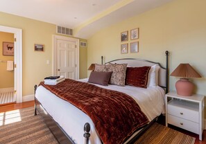 Ein Schlafzimmer mit Bett, Nachttischen, einer Tür und Wandbildern.