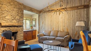 Een gezellige woonkamer met een stenen muur, houten lambrisering, een open haard, een bank en een salontafel.