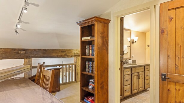 Een kamer met een houten boekenkast, een eettafel met stoelen en uitzicht op een balkon.