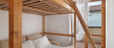 Una habitación con una cama nido de madera, una ventana con cortinas blancas y vistas al exterior.