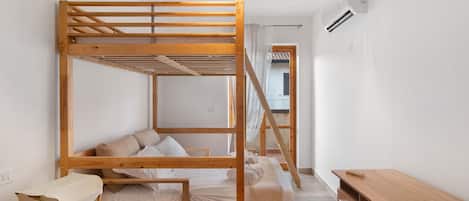 A minimalist room with a wooden bunk bed, a small desk, and a hanging light fixture.
