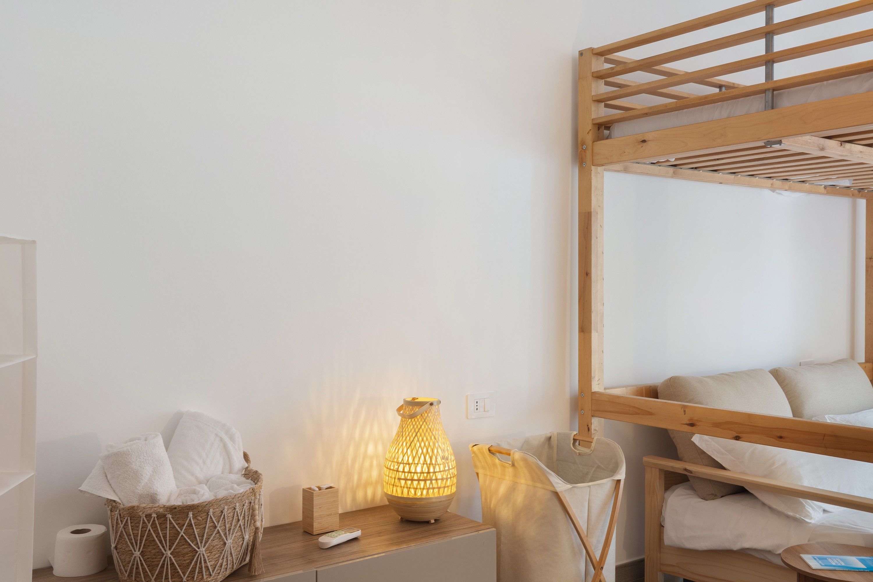 Ein Stockbett mit Holzrahmen, eine Nachttischlampe, eine Taschentuchbox und ein Korb mit Handtüchern.