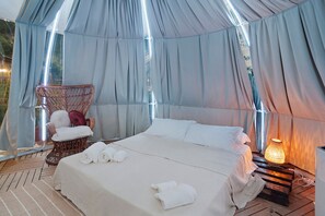 Un alloggio in tenda con un letto, una sedia in vimini e un tavolo con una lampada.