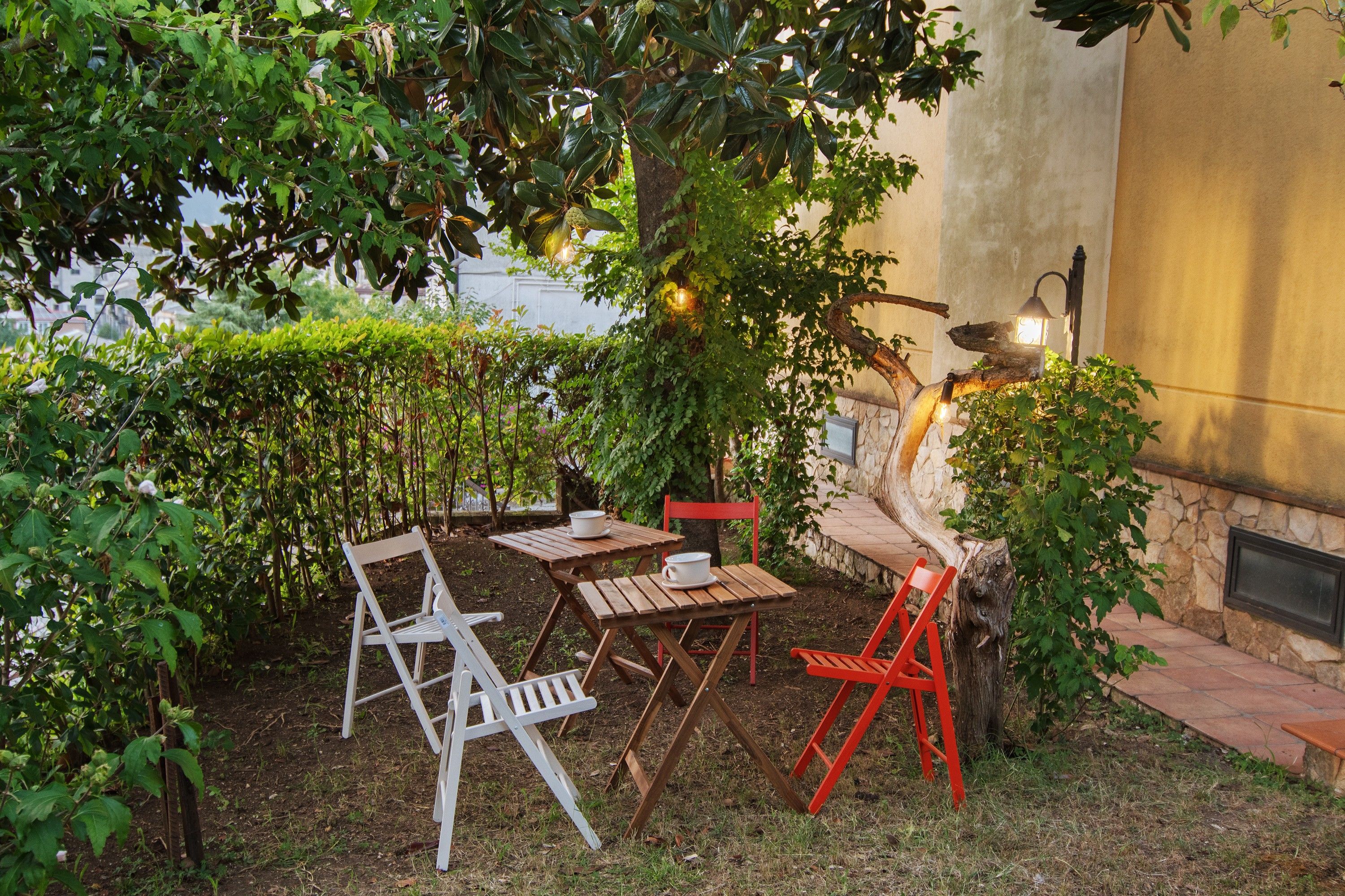Un área de estar al aire libre con una mesa y sillas, rodeada de follaje y un muro de piedra.