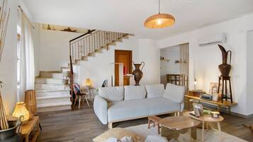 Un salon spacieux avec un escalier, un canapé, une table basse et un luminaire suspendu.