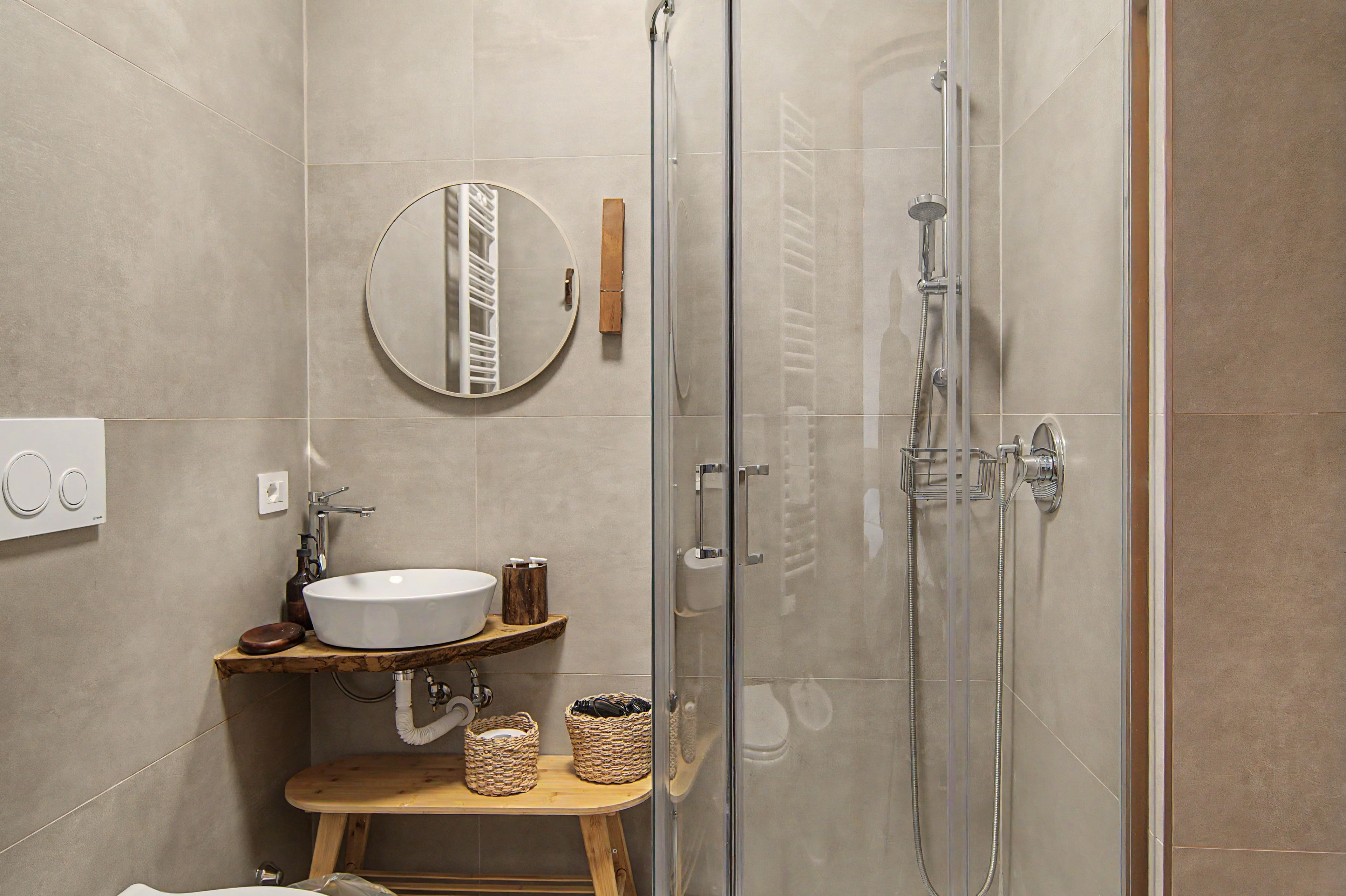Une salle de bain moderne avec une douche à parois de verre, un miroir rond et un meuble-lavabo en bois.