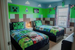 Ein Schlafzimmer mit zwei Betten, jedes mit einer Minecraft-Decke, einem Fenster mit Vorhängen und einer Wand mit Minecraft-Muster.