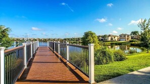 A wooden bridge leading to a residential area with houses and a body of water. - Go!#13 WINDSOR AT WESTSIDE (Kissimmee)