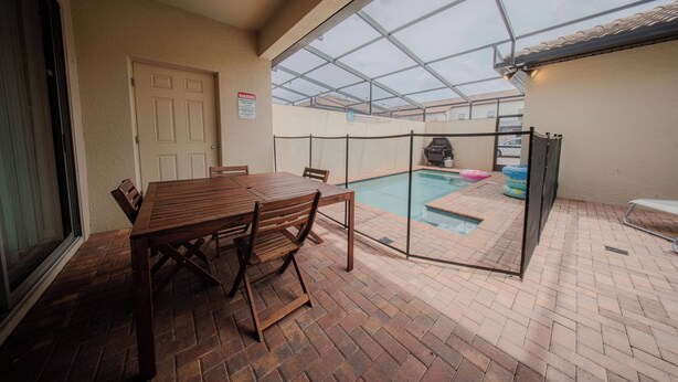 Un portico coperto con una piscina, un tavolo di legno e delle sedie.