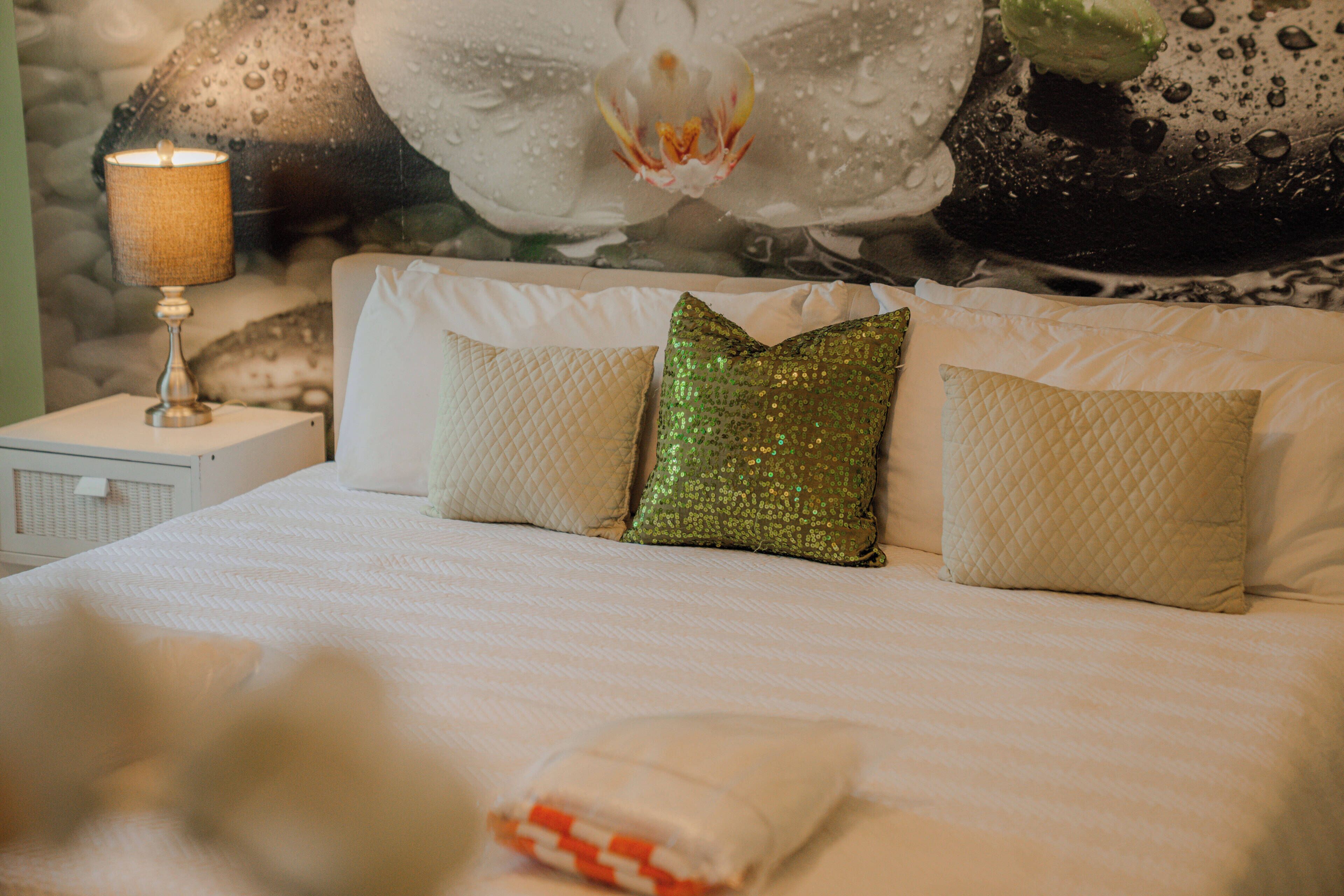 Un lit avec une literie blanche, un oreiller matelassé et un oreiller orné de paillettes.