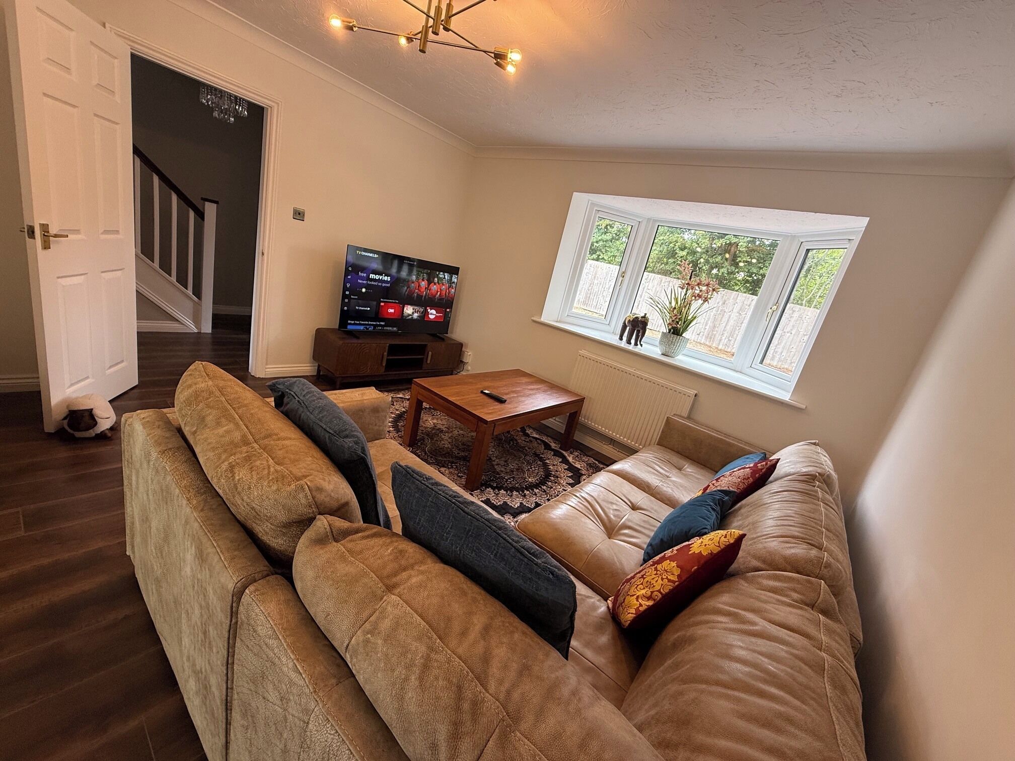 A living room with a leather sofa, a coffee table, a TV, and a window with a view of greenery.