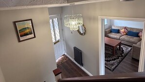 A staircase leading to a living area with a chandelier, a framed picture, and a view of a sofa and coffee table.