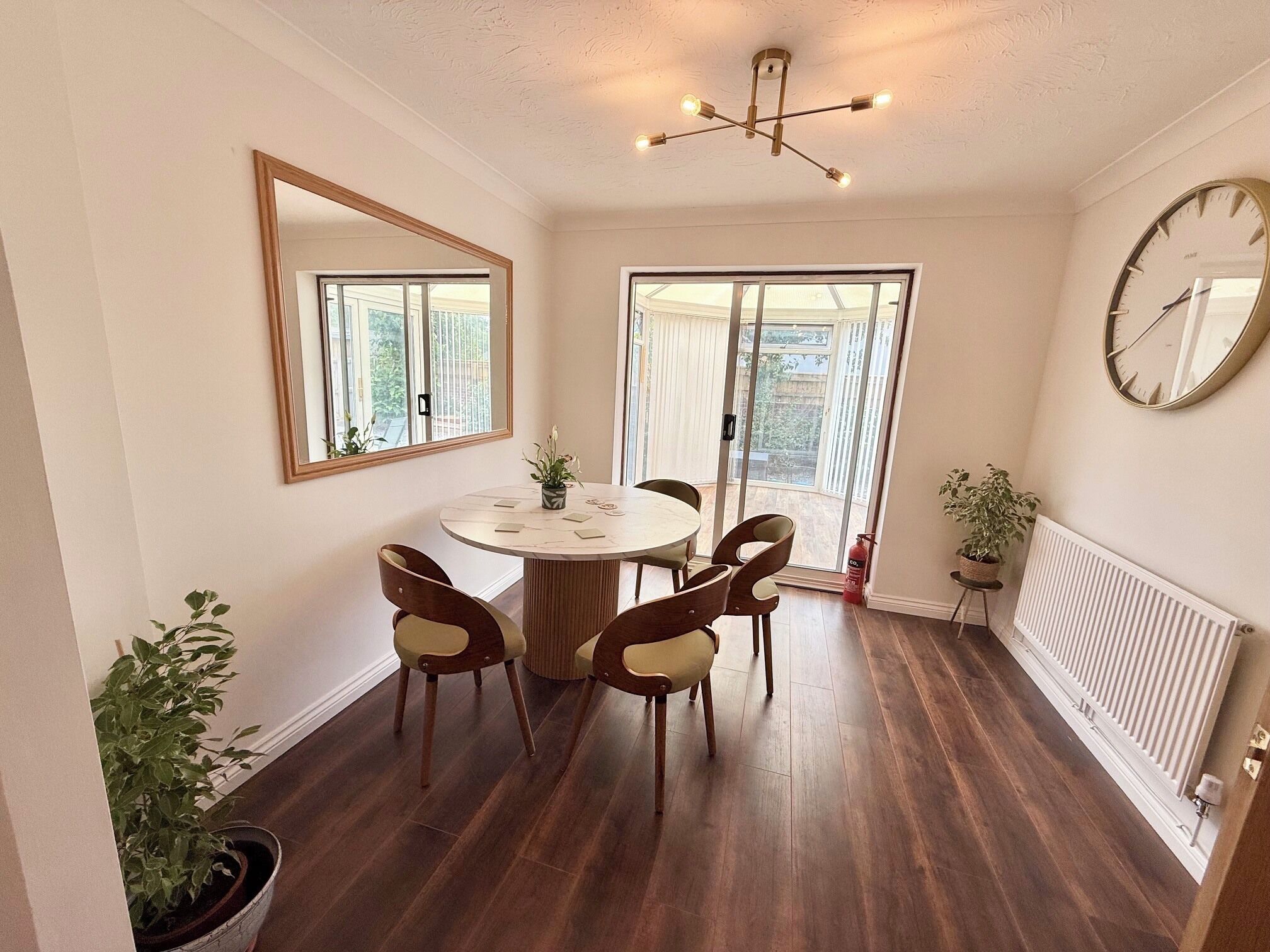 A dining area with a round table, four chairs, a ceiling light fixture, and a large mirror on the wall.