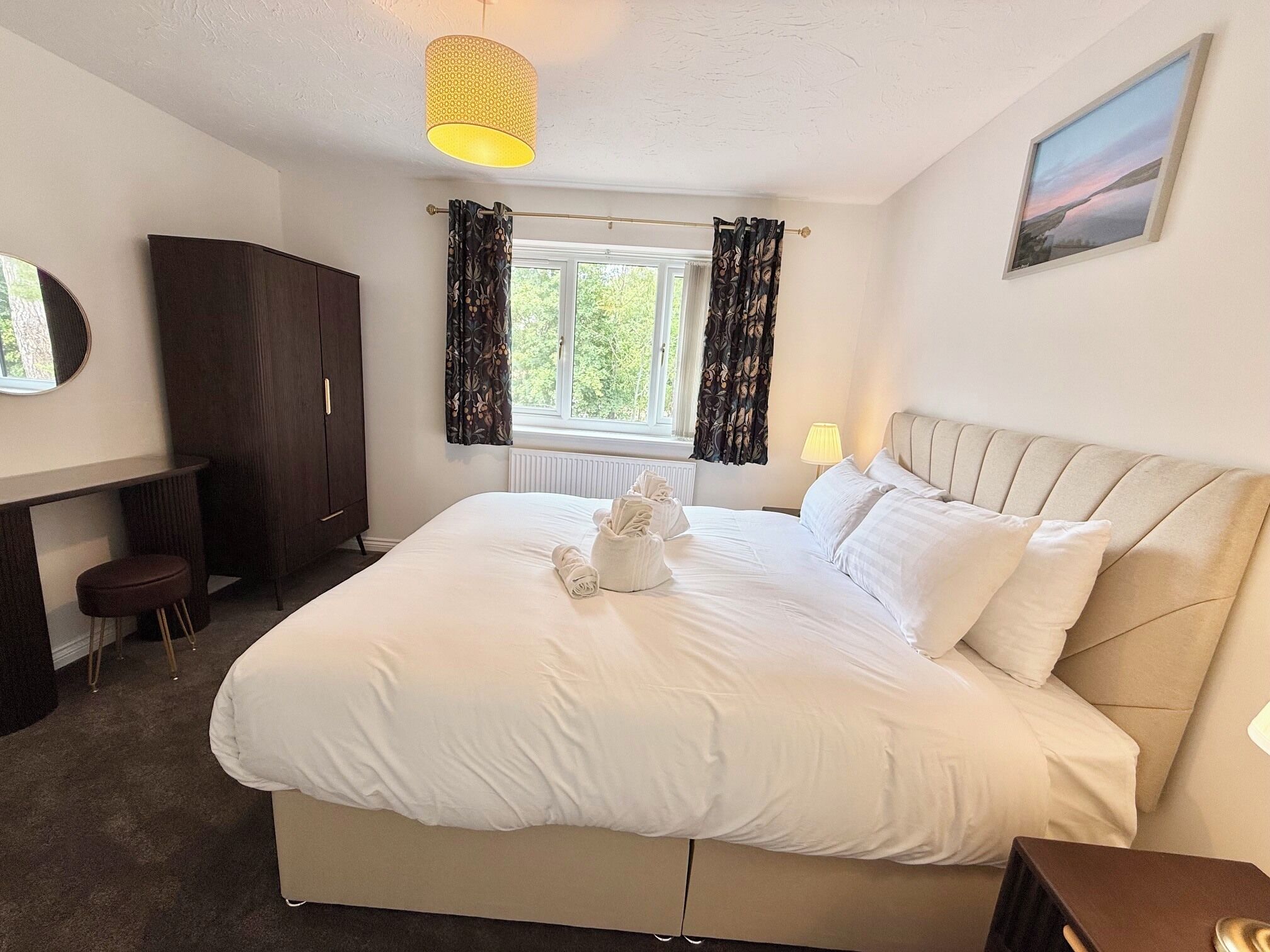 A hotel room with a bed, a desk, a wardrobe, a window with curtains, and a painting on the wall.