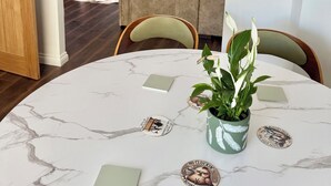 A dining area with a round table, chairs, a potted plant, and decorative coasters.