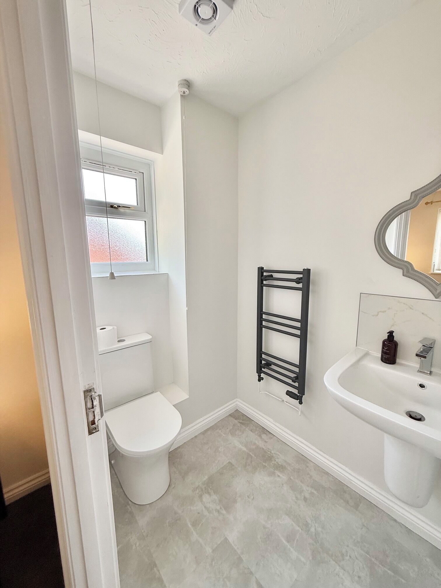 A bathroom with a toilet, a towel rack, a sink, and a mirror.