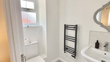 A bathroom with a toilet, a towel rack, a sink, and a mirror.