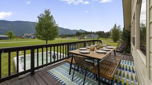 Eine Terrasse mit Esstisch, die auf eine Wiese mit Bergen im Hintergrund blickt.