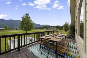 Eine Terrasse mit Esstisch, die auf eine Wiese mit Bergen im Hintergrund blickt.