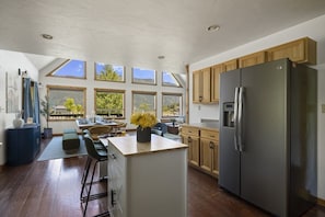 A modern kitchen with a central island, wooden cabinets, and a stainless steel refrigerator.