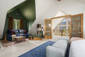 Ein Schlafzimmer im Loft-Stil mit schräg verlaufender Decke, einem großen Fenster und Blick ins Freie.