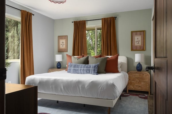 A bedroom with a bed, two bedside tables, a window with curtains, and framed pictures on the wall.
