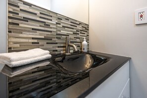 A modern bathroom with a black sink, a glass backsplash, and a white towel on the counter. - Charming 1BD Getaway - Unwind Near Niagara Falls (Niagara Falls)