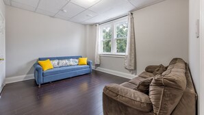 Ein Zimmer mit einem blauen und einem braunen Sofa, einem Fenster mit Vorhängen sowie einer weißen Decke mit Einbaustrahlern.