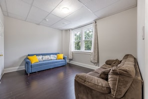 Ein Zimmer mit einem blauen und einem braunen Sofa, einem Fenster mit Vorhängen sowie einer weißen Decke mit Einbaustrahlern.