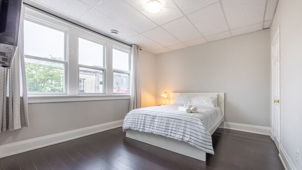 Ein Schlafzimmer mit großem Fenster, einem Bett mit gestreifter Bettdecke, einer Nachttischlampe und einem dunklen Holzboden.
