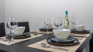 Ein Esstisch ist gedeckt mit weißen Schüsseln, blauen Tellern und klaren Weingläsern, mit einer Flasche Weißwein und einem Korkenzieher darauf.