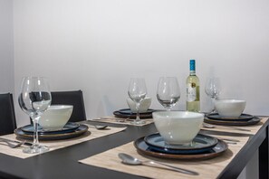Ein Esstisch ist gedeckt mit weißen Schüsseln, blauen Tellern und klaren Weingläsern, mit einer Flasche Weißwein und einem Korkenzieher darauf.